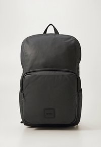 Crni najlonski ruksak pravokutnog oblika, s prednjim džepom na patentni zatvarač i gornjom drškom. Na prednjoj strani nalazi se logotip.