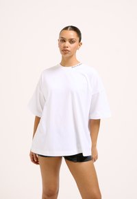 Valget puuvillane suurte mõõtudega T-särk, millel on lühikesed varrukad ja ümar kaelus, krael trükitud brändinimega.