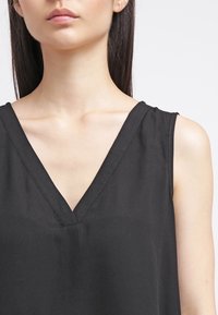 Svart ärmlös topp med en djup V-ringning och slät textur. Tyget verkar lätt med en enkel, ren design.