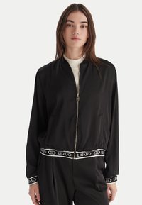 Giubbotto bomber nero in tessuto elegante con zip frontale, polsini a coste e vita con logo Liu Jo a contrasto.