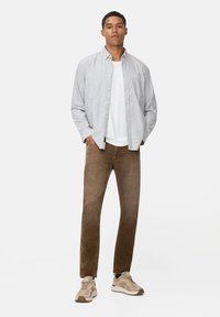 Gestreepte button-up shirt in blauw en wit, gecombineerd met een wit T-shirt en een bruine broek. Beige sneakers met textuuraccenten maken de look compleet.