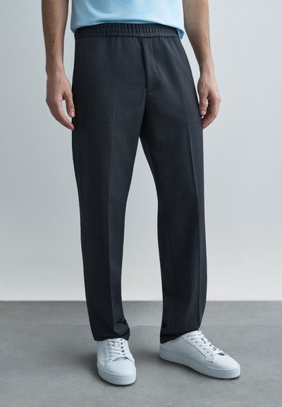Pantaloni grigio scuro con cintura elastica, design a gamba dritta, texture sottile, abbinati a sneakers bianche.