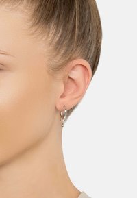 Pendiente de aro de plata con formas abstractas y detalles troquelados. El diseño es elegante y moderno con un acabado pulido.