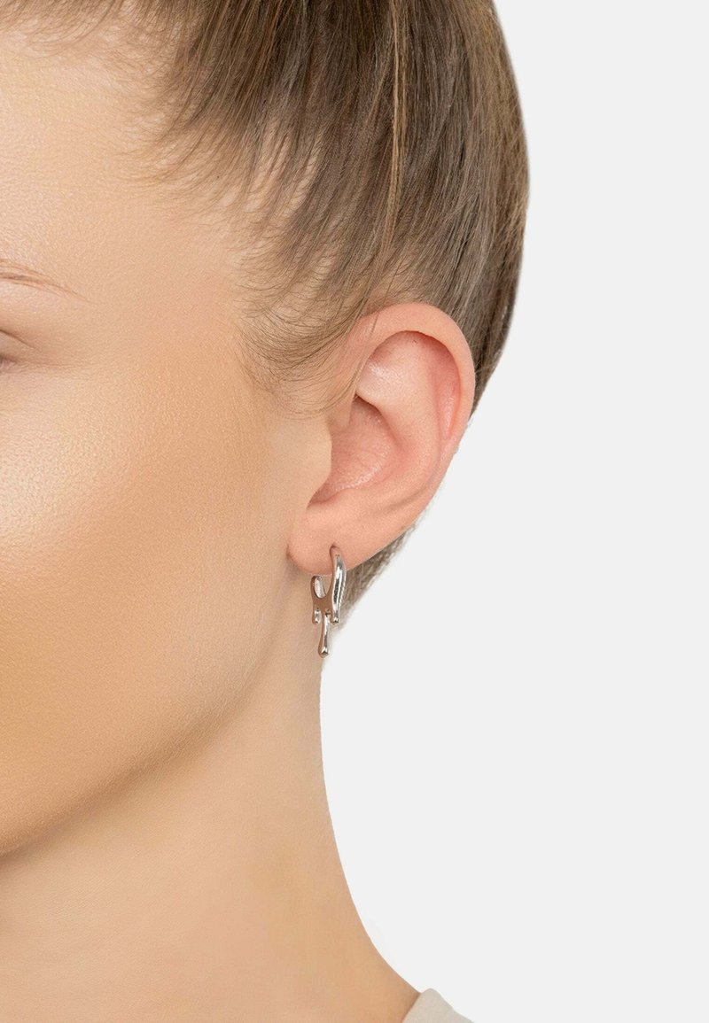 Pendiente de aro de plata con formas abstractas y detalles troquelados. El diseño es elegante y moderno con un acabado pulido.