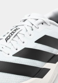 Close-up of white Adidas running shoe with black stripes and "ADIZERO" text on the tongue.