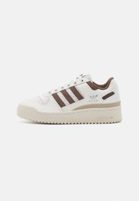 White leather sneaker with brown accents, featuring three lateral stripes, a textured sole, and perforated detailing on the toe cap.