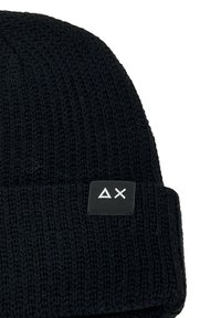 Berretto di maglia nero con risvolto e un'etichetta rettangolare nera con un logo geometrico bianco. Materiale caldo e texturizzato.