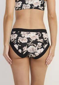 Blommönstrade svarta trosor med spetskant. Tyget är slätt och mjukt, med stora rosa och krämfärgade blommor mot en mörk bakgrund.