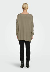 Olivenfarbener, oversized Pullover mit weitem Ausschnitt und langen Ärmeln, kombiniert mit schwarzen Skinny Jeans und Ankle Boots. Weiches, strukturiertes Material.