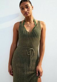 Abito in maglia verde oliva con scollatura a V, spalline sottili e cintura con nodo. Presenta un motivo a righe verticali testurizzate. Leggero, con silhouette aderente.