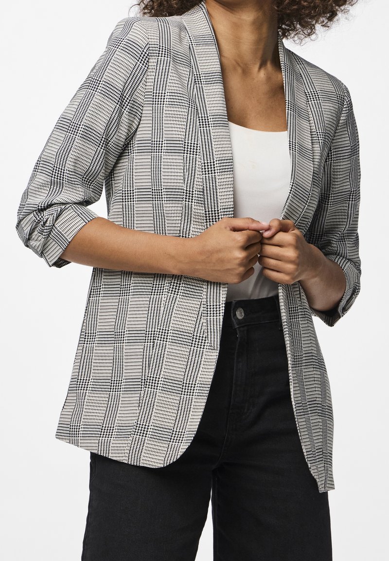 Svartvitt rutigt kavaj med notchade slag och trekvartärmar, bärs över en vit topp och parats med svarta byxor.