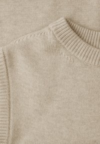 Gros plan sur un pull beige en maille, avec un col rond côtelé et un tissu doux et texturé agrémenté de détails de couture lisse.