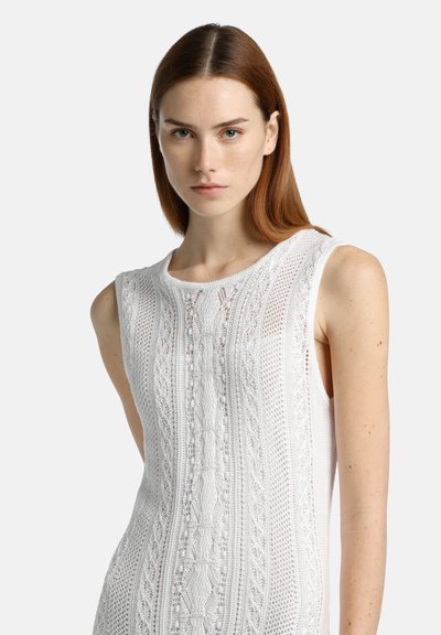 Vestido sin mangas blanco que presenta intrincados patrones de punto, un cuello redondo y una tela texturizada con secciones transparentes.