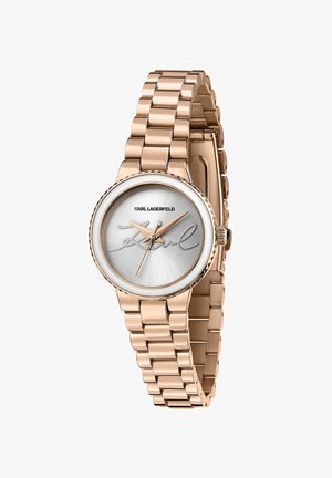 Montre en or rose avec un bracelet métallique à maillons, dotée d'un cadran argenté et d'un détail signature. Boîtier rond avec une lunette texturée et des index simples.