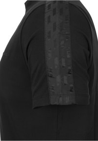 Svart kortärmad skjorta med en texturerad svart panel på vänster axel. Tyget är mjukt och har en slät finish.