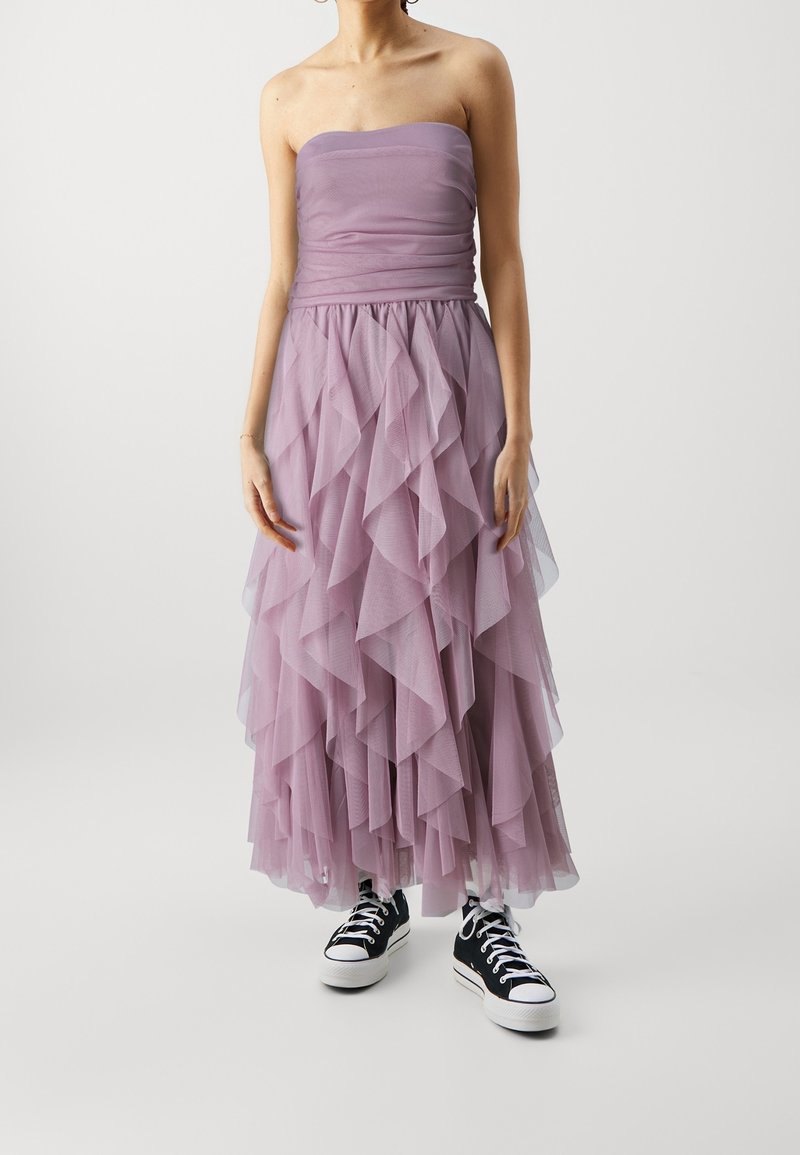Robe lilas sans bretelles avec des volants en tulle superposés, dotée d'un corsage ajusté et d'une taille élastique, associée à des baskets noires.