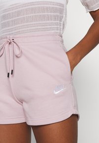 Vaaleanpunaiset Nike-shortsit pehmeästä kankaasta, joissa on joustava vyötärönauha, kiristysnyöri, sivutaskut ja jalassa kirjailtu logo.
