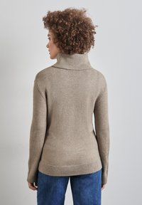 Béžový rolák se žebrovaným límcem a manžetami, jemná textura, přiléhavý střih a mírně delší zadní část, spárovaný s džíny.