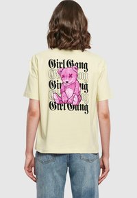 Geltonas medvilninis tinklinis marškinėliai su rausvos spalvos lokio grafika ir juodu užrašu "Girl Gang" pakartotinai. Laisvas kirpimas, trumpomis rankovėmis ir apvaliu iškirpimu.