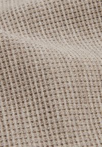 Material textil bej cu textură, prezentând un model în grilă, cu pătrățele proeminente și ridicate. Moale și țesut, potrivit pentru diverse aplicații textile.