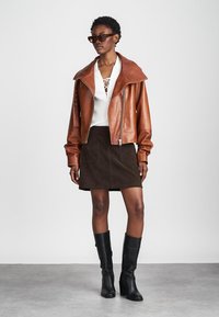 Brown leather cropped jacket with large collar, white lace-up top, brown suede skirt with pockets, and knee-high black boots.