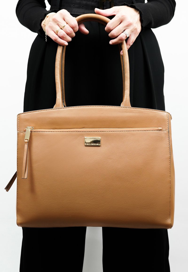 Tan leren handtas met een ritsvak aan de voorkant, gouden hardware en twee korte handvatten. Glad texuur en rechthoekige vorm.