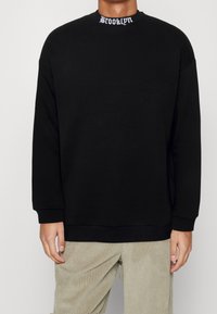 Felpa nera con maniche lunghe, vestibilità rilassata. Presenta un colletto a coste con "Brooklyn" ricamato in bianco. Tessuto liscio, design minimalista.