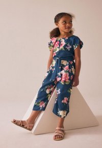 Mornarsko modr kombinezon s kratkimi rokavi, pasom in skrajšanimi hlačnicami. Na njem so rožnate in bele cvetlične vzorce. Svetlo rožnate sandale z zankami.