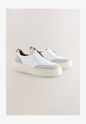 Valkoiset nahkaiset slip-on-kengät, joissa on harmaat mokkanahkaiset yksityiskohdat, paksu kermanvärinen pohja ja hienovaraiset ompeluvarit koko mallissa.