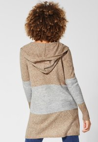 Pletený cardigan s kapucí, s designem v hnědých a šedých blocích barev, žebrovanými manžetami a volným střihem, vyrobený z měkkého texturovaného materiálu.