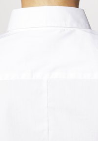 Vista posteriore di una persona che indossa una camicia bianca impeccabile con colletto standard e una cucitura centrale sulla parte superiore della schiena.