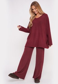 Burgundowy zestaw wypoczynkowy składający się z luźnej bluzki z szerokimi rękawami oraz pasujących spodni z szerokimi nogawkami, wykonany z miękkiego, teksturowanego materiału.