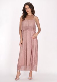 Rochie maxi dintr-un material roz deschis, cu un top stratificat, bretele fine și o textură strălucitoare. Asortată cu sandale cu toc înalt argintii.