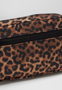 Pochette en tissu imprimé léopard avec fermeture éclair noire, présentant un gros plan détaillé du motif texturé et des coutures.