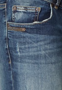 Blue denim jeans with faded areas, a small back pocket, and copper-tone hardware. Features subtle stitching and a classic cut.