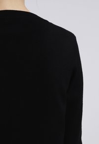 Maglione nero a maglia con design semplice a girocollo e texture liscia, vista posteriore con dettagli sulle cuciture delle spalle.