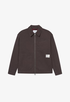 Brown cotton jacket with a collar, front zipper, two large pockets, and a small chest pocket. Label detail on the lower pocket.