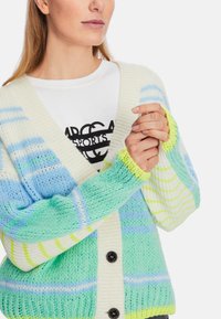 Knit cardigan in pastel green, blue, and white stripes, featuring a v-neck, large buttons, and ribbed cuffs with yellow accents.