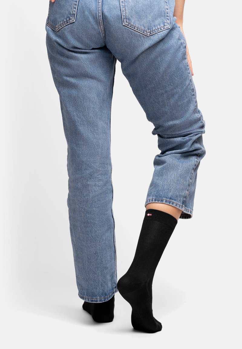 Calcetines negros hasta la rodilla con un pequeño logo rojo y blanco en el puño, usados con unos vaqueros de denim de color azul claro, que cuentan con un ajuste relajado y un diseño clásico.