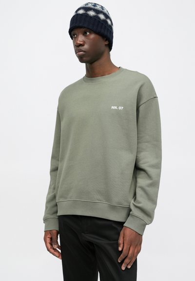 Olijfgroene sweatshirt met ronde hals, ribgebreide manchetten en zoom. Heeft een wit "NN. 07" logo op de borst. Gdraagd met zwarte broek.
