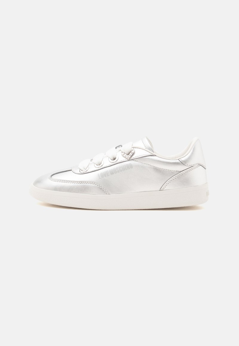 Άσπρο sneaker χαμηλού τύπου με γυαλιστερό φινίρισμα, με το λογότυπο "Love Moschino" στο πλάι, κλείσιμο με κορδόνια και μεταλλική καρδιά κοντά στα κορδόνια.