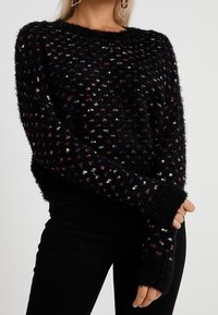 Czarny, puszysty sweter z wielokolorowymi drobinkami, okrągłym dekoltem i długimi rękawami z żebrowanymi mankietami. Miękka tekstura i luźne dopasowanie.