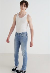 Lys blå denim bukser med slim fit, kombinert med en hvit tank topp og svarte sko. Buksene har vanlige lommer og sømdetaljer.