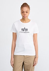 T-shirt en coton blanc à manches courtes, doté d'un logo noir "Alpha Industries" et d'un design géométrique au centre.