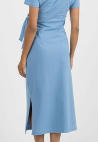 Hellblaues, kurzärmliges Kleid aus weichem Stoff. Es hat ein Wickeldesign mit einem Gürtel in der Taille und einem seitlichen Schlitz für mehr Bewegungsfreiheit.