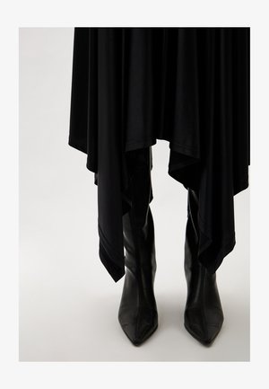 Black, flowing dress with a high-low hem, paired with sharp, pointed black leather boots. Soft texture, no visible patterns or accents.