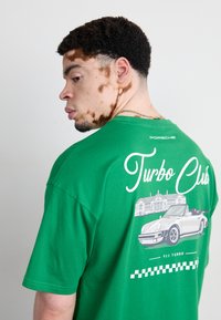 Grøn bomulds-T-shirt med et grafik af en Porsche 911 Turbo og "Turbo Club"-tekst på ryggen, med en afslappet pasform og korte ærmer.