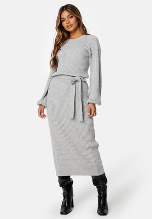 Graues geripptes Strickkleid mit langen Ärmeln und einem Bindegürtel in der Taille; kombiniert mit kniehohen schwarzen Stiefeln. Strukturierter Stoff.