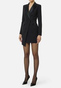Abito blazer aderente nero con rever in raso, doppiopetto con bottoni e silhouette sagomata, abbinato a calze nere trasparenti e décolleté con punta.