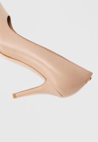 Décolleté beige con tacco alto in pelle liscia, punta affilata e tacco a spillo sottile. Design distintivo con ritagli sui lati.